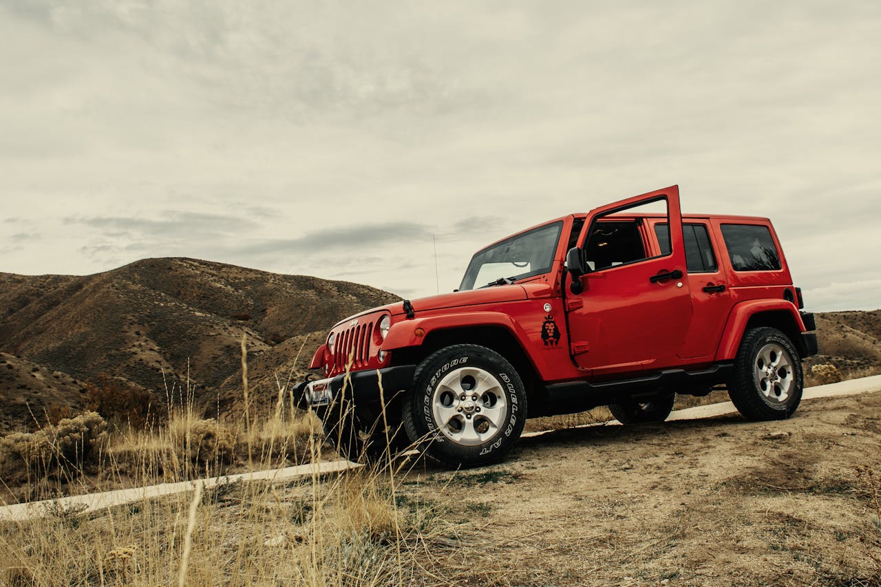 A vibrant red SUV parked on a dirt road with a mountain landscape backdrop under a cloudy sky.