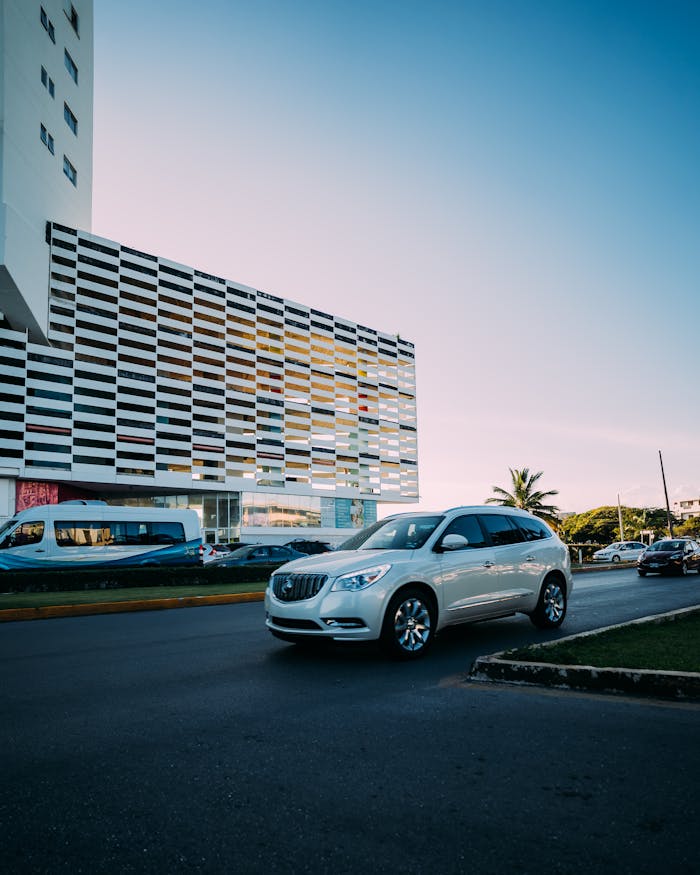 Modern SUV driving past architectural facade in an urban setting during twilight.