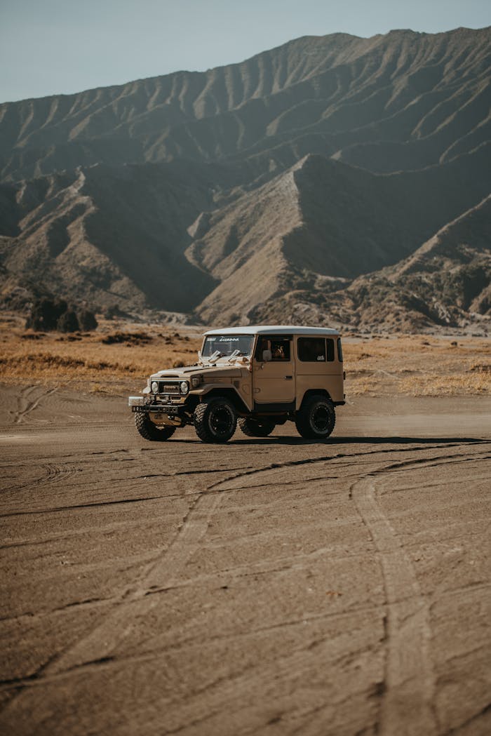 A rugged vintage SUV traverses an arid desert terrain with majestic mountain backdrops.